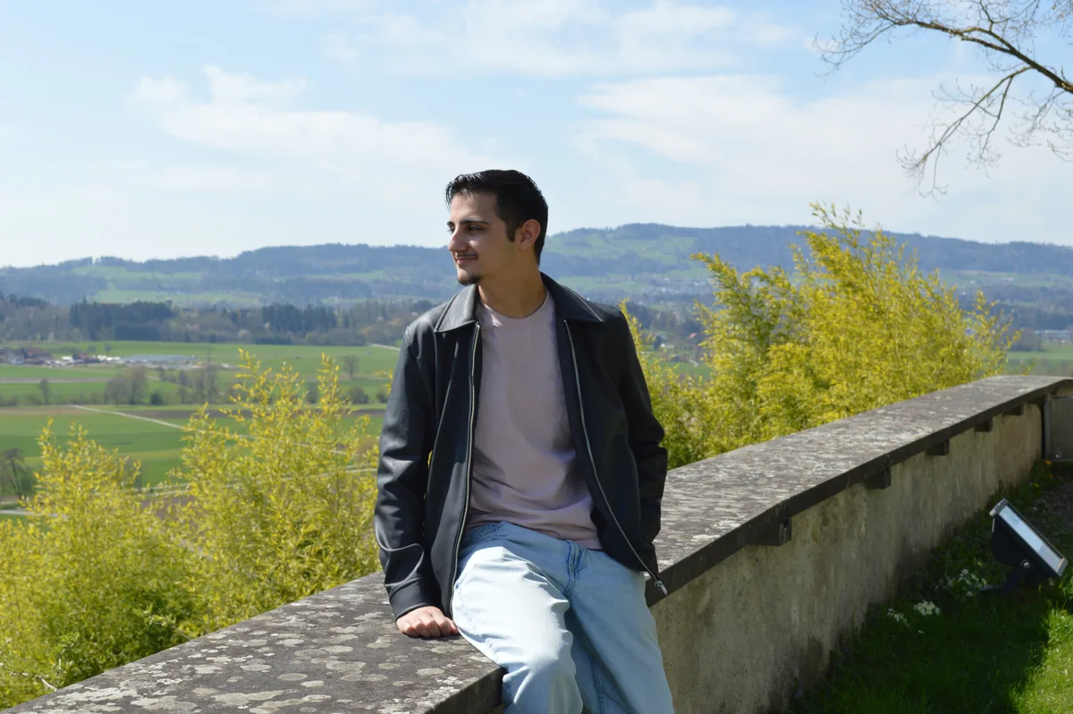 Jules sitzt auf einer Mauer, im Hintergrund die Berge, die Sonne scheint.